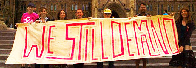 big sign "we still demand". Lots of protesting people